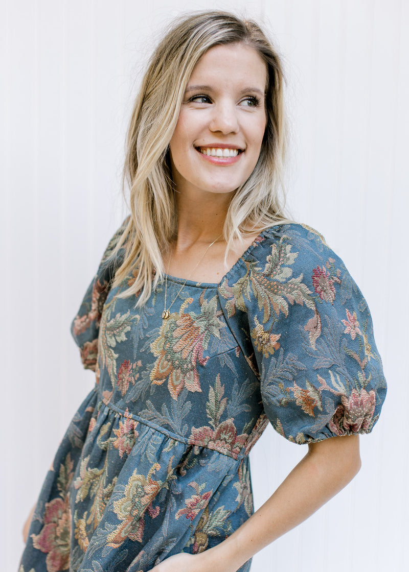 Close up of a square neck and bubble short sleeves on a model in a blue dress with floral stitching.