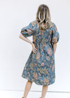 Back view of Model wearing a blue midi dress with floral stitching  and bubble short sleeves. 