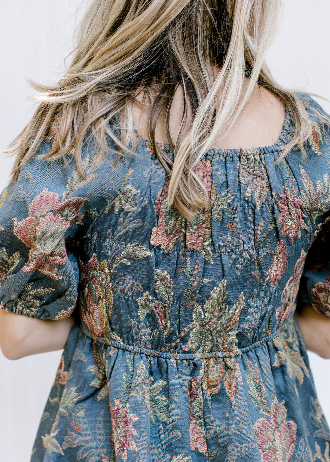 Close up of square neckline and ruched fabric on the back of a blue dress with floral stitching.