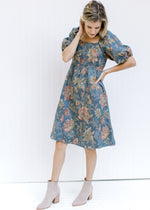 Model wearing a blue dress with floral stitching, a square neckline and bubble short sleeves. 