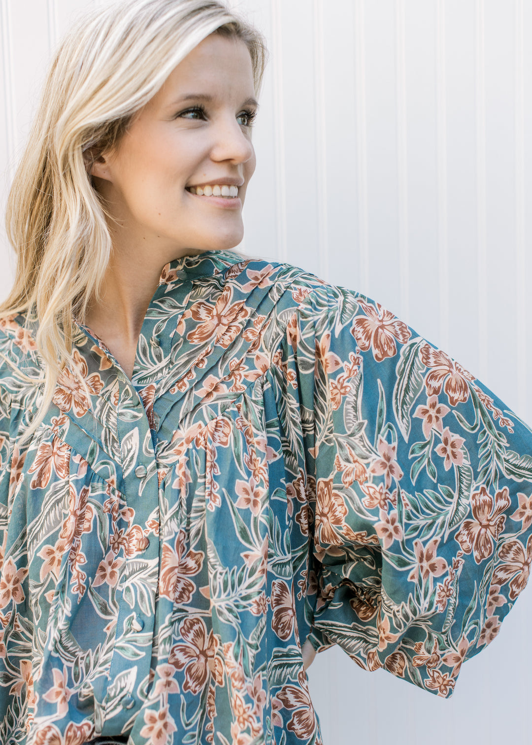 Close up of pleated yolk and covered buttons on a teal long sleeve top with flowers. 