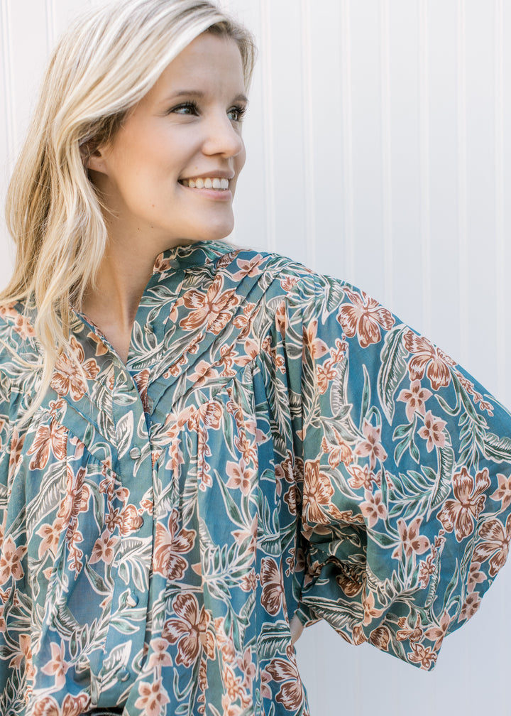 Close up of pleated yolk and covered buttons on a teal long sleeve top with flowers. 
