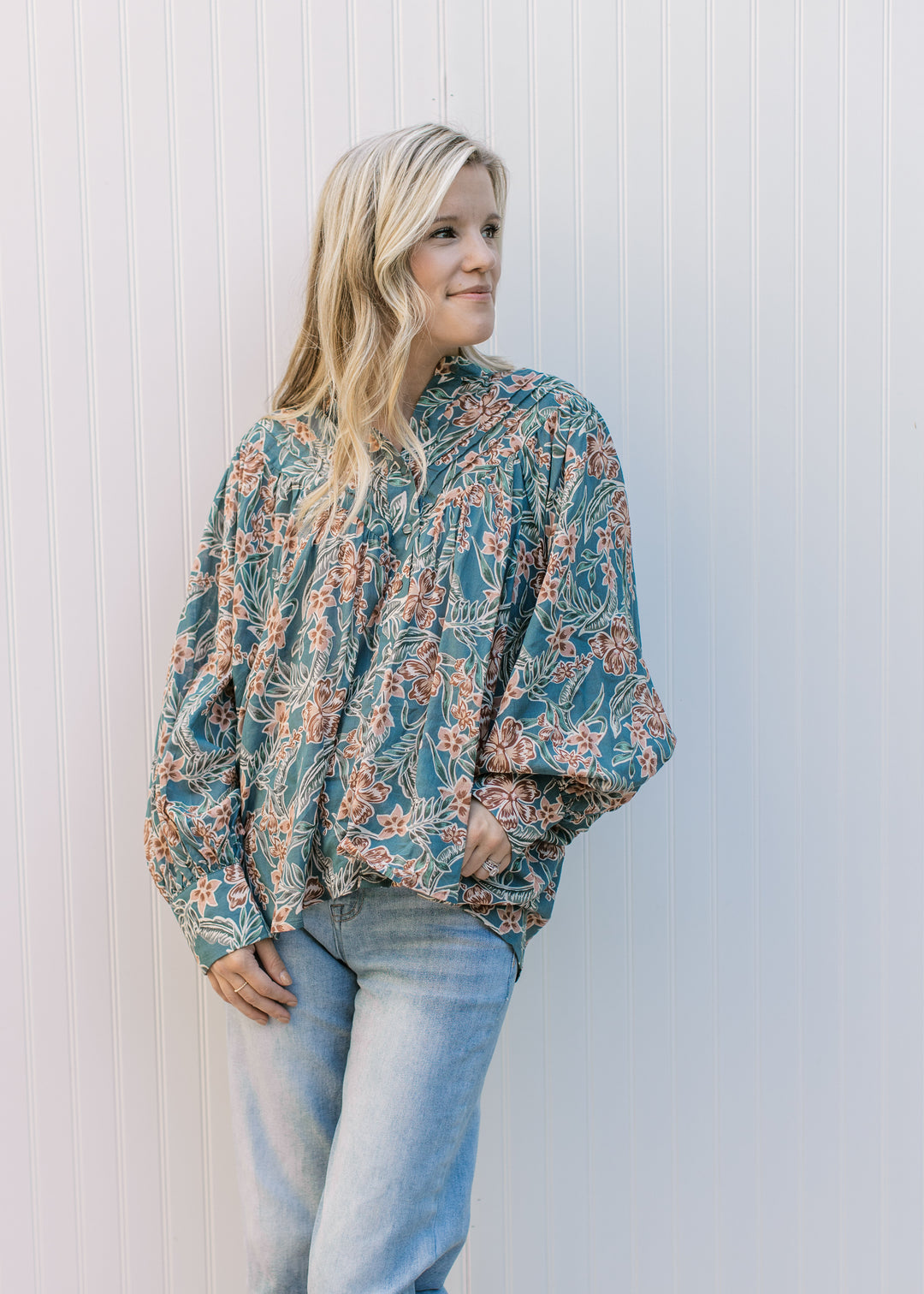 Model wearing a teal top with flowers, bubble long sleeves, covered button front and pleated yolk. 