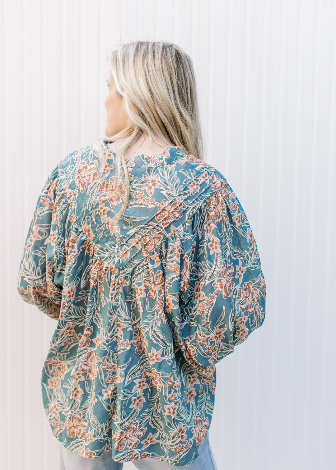 Back view of Model wearing a teal top with flowers, bubble long sleeves and pleated yolk. 