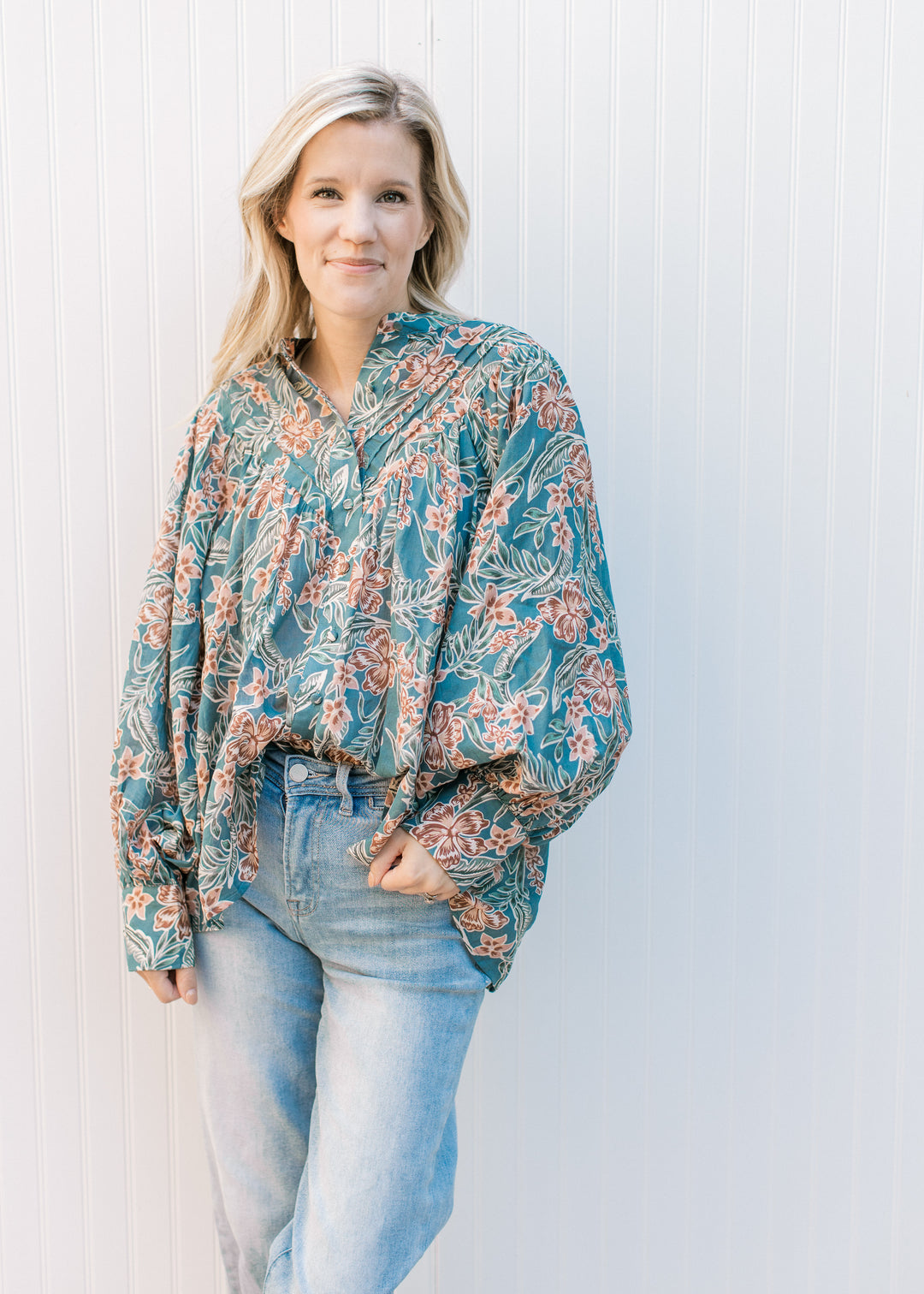Model wearing jeans and a teal top with flowers, bubble long sleeves, button front and pleated yolk.