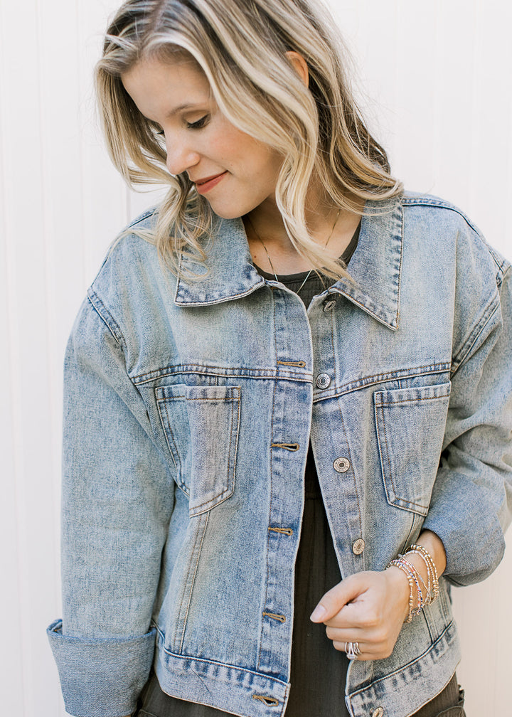 Model wearing a button up, light wash denim jacket with long sleeves and patch pockets. 