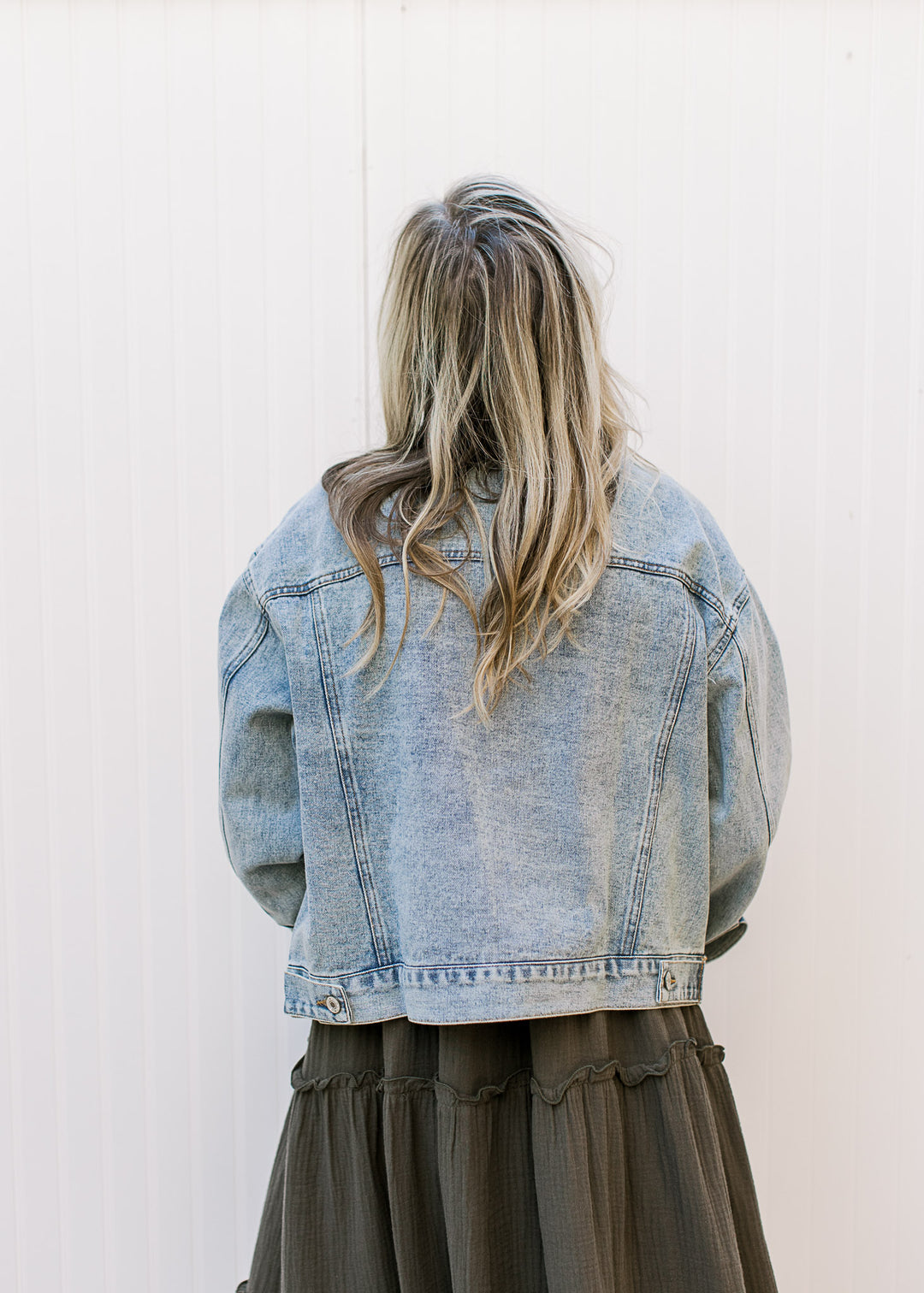 Back view of Model wearing a light wash denim jacket with long sleeves and patch pockets. 