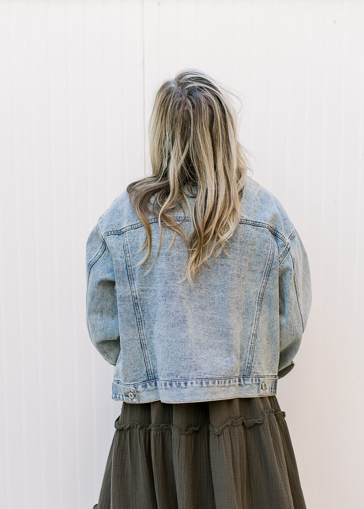 Back view of Model wearing a light wash denim jacket with long sleeves and patch pockets. 
