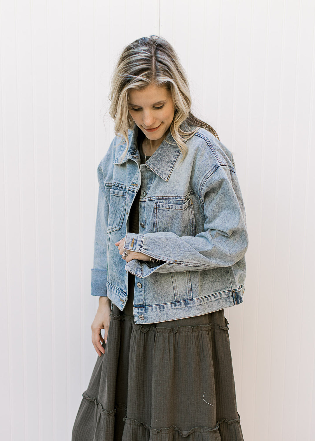Model wearing a button up, light wash denim jacket with long sleeves and button cuffs. 