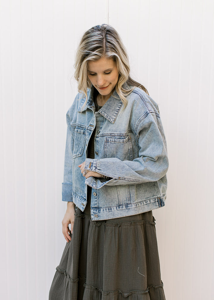 Model wearing a button up, light wash denim jacket with long sleeves and button cuffs. 