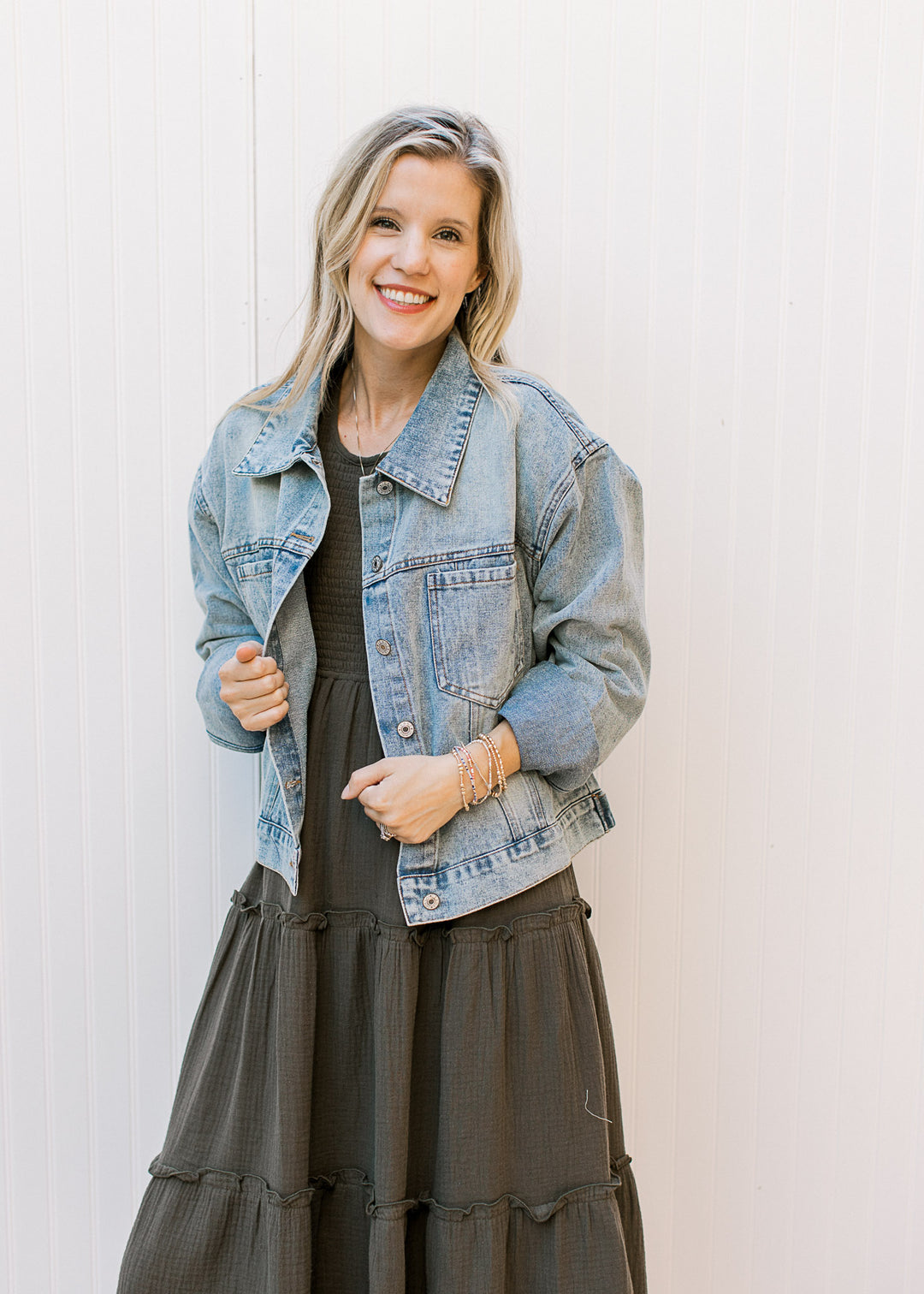 Model wearing a button up, light wash denim jacket with long sleeves and flap collar. 