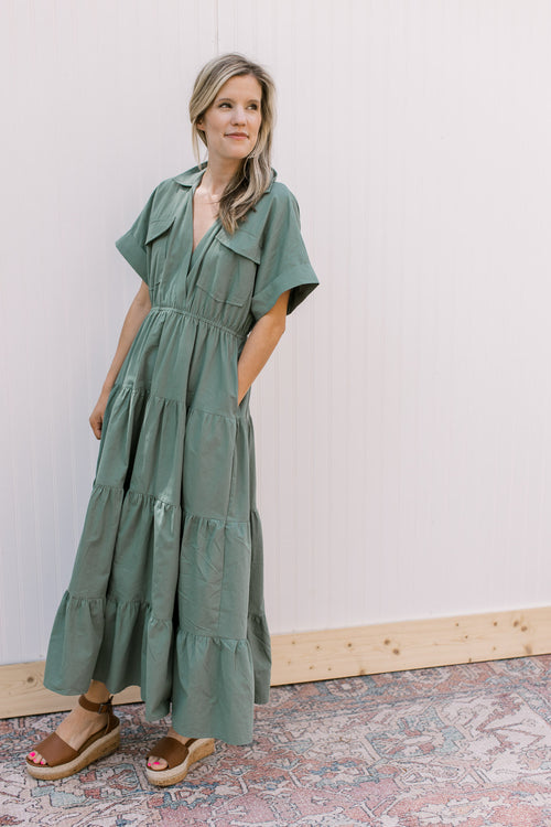 Model wearing a tiered green dress with patch pockets, v-neck and short sleeves. 
