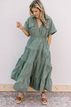 Model wearing a tiered green cotton dress with patch pockets, v-neck and short sleeves.