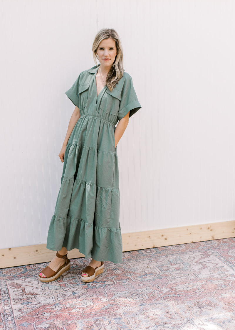 Model wearing a tiered green dress with pockets, v-neck and short sleeves.