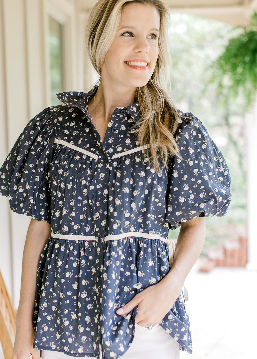 Model wearing a navy top with white flowers, short puff sleeves, button font and side tie detail.