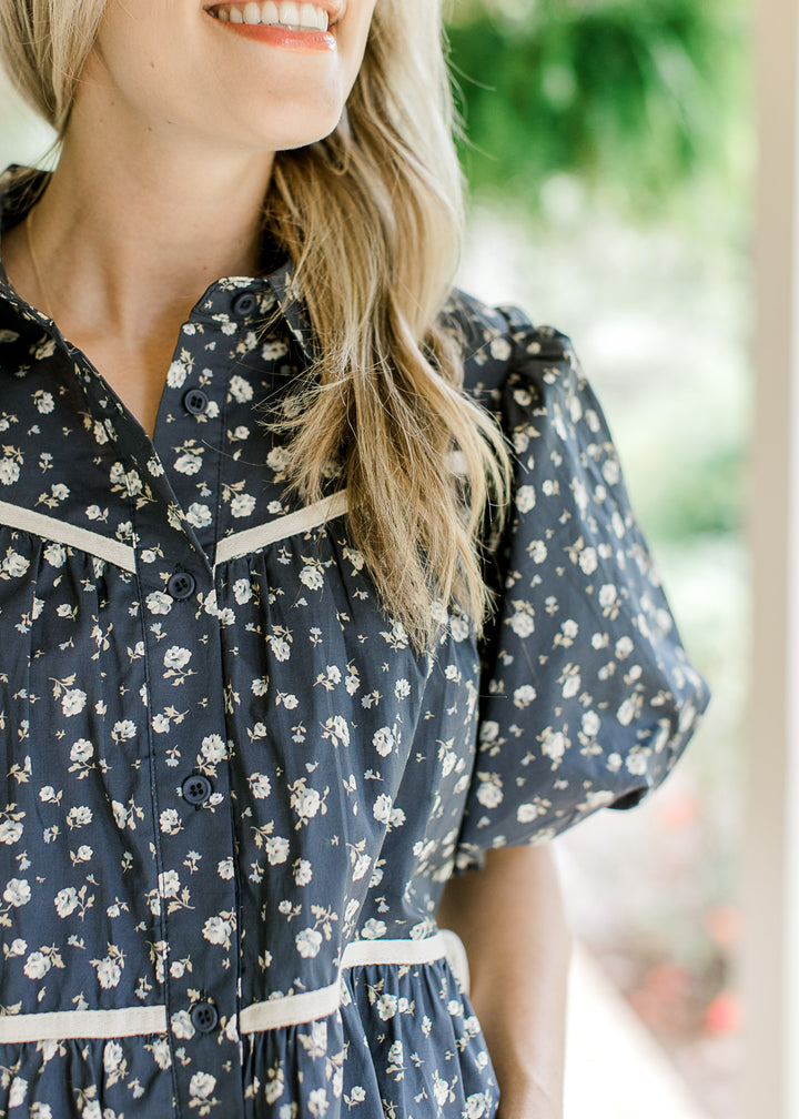 Close up of pleating detail and buttons on the front of a navy top with white flowers. 
