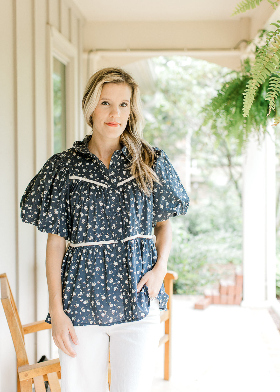 Model wearing white pants with a navy top with white flowers, short puff sleeves and a button font.