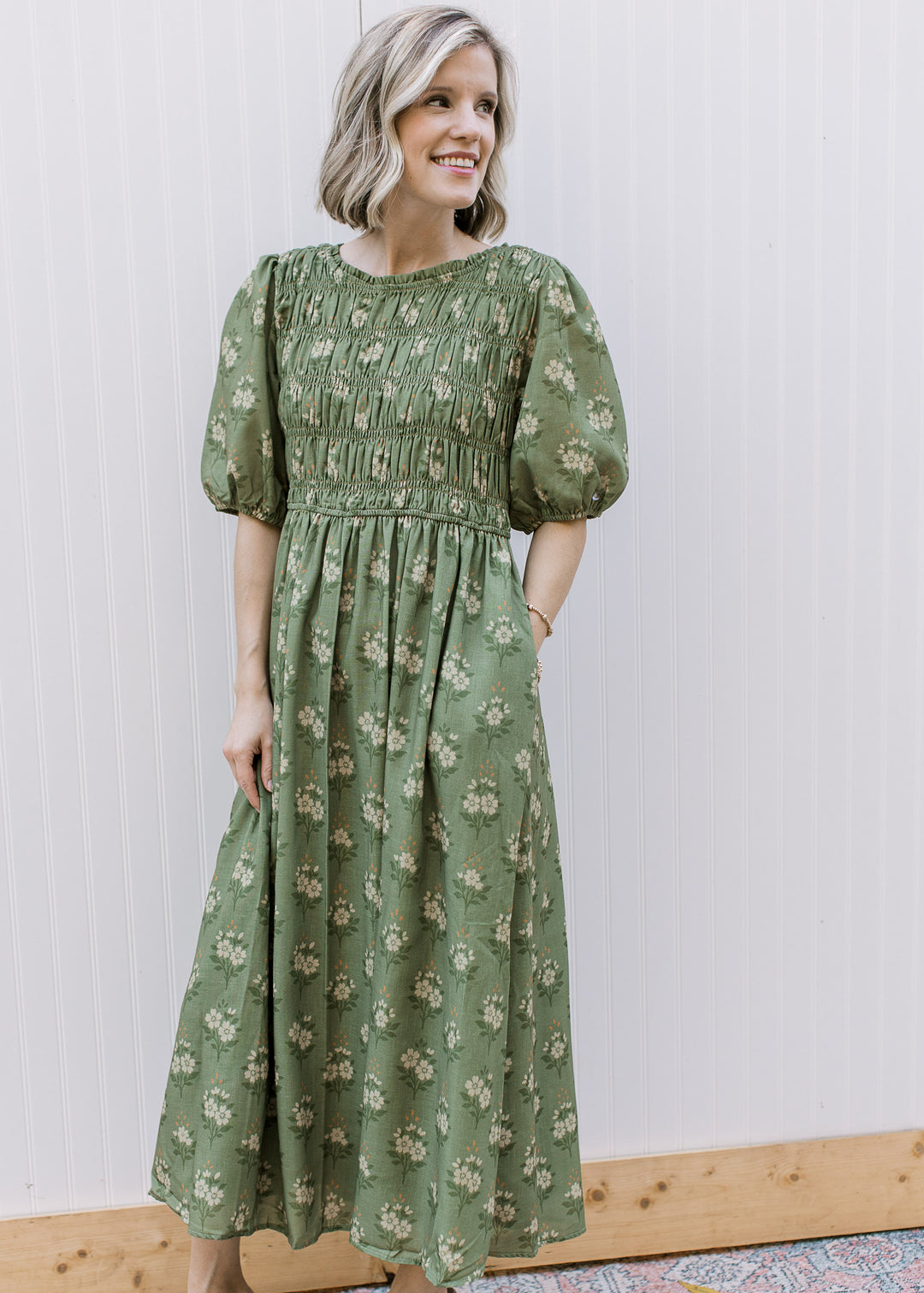 Model wearing an olive midi with cream floral, smocked bodice, pockets and elbow-length sleeves. 