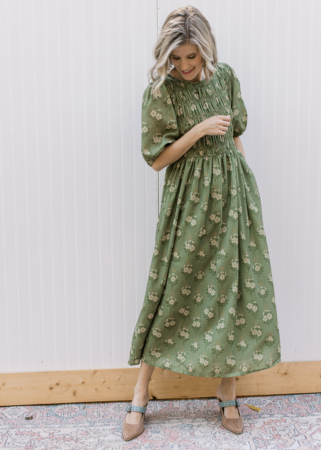 Model wearing an olive midi with cream floral, smocked bodice, flowy skirt and elbow sleeves. 