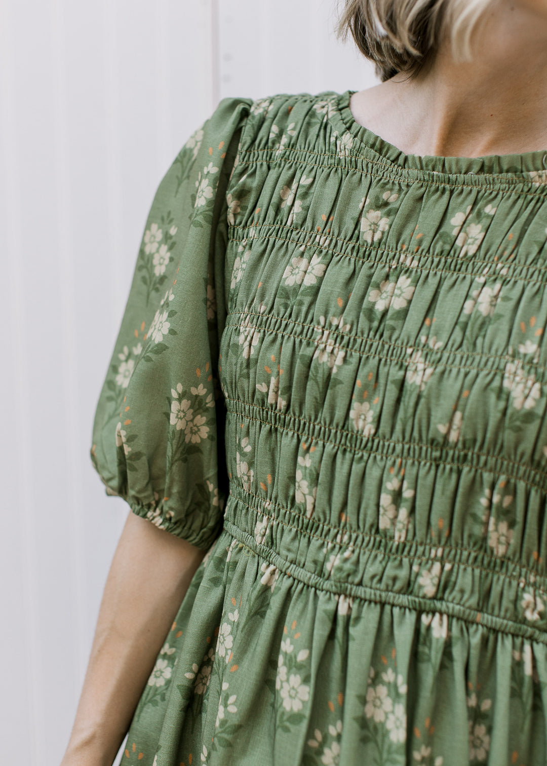 Close up of smocked bodice and elbow length sleeves on an olive midi with cream floral. 