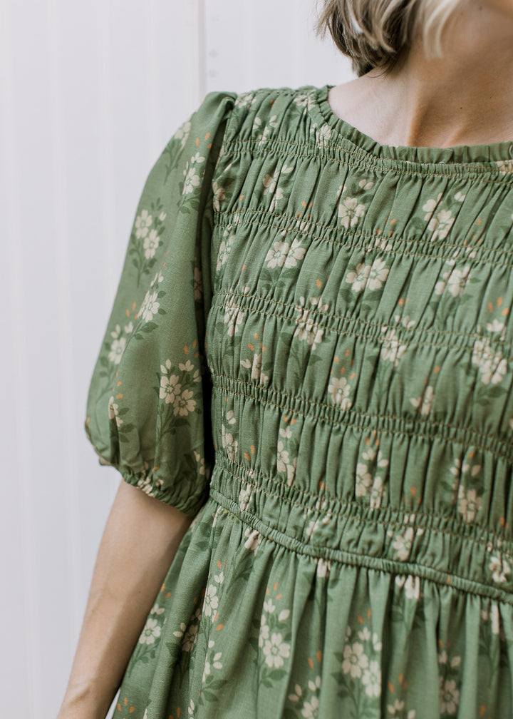 Close up of smocked bodice and elbow length sleeves on an olive midi with cream floral. 