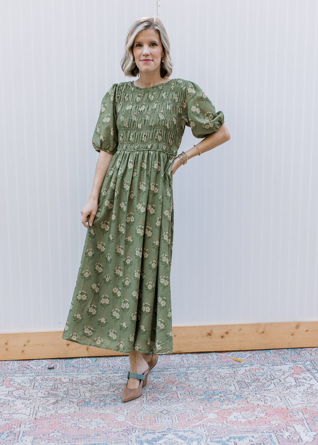 Model wearing an olive midi with cream floral, smocked bodice, pockets and elbow sleeves. 