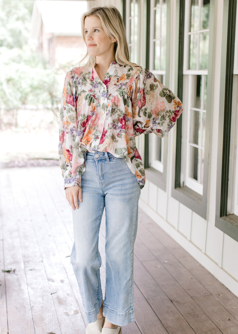 Model wearing a floral long sleeve top with a pleated bodice, covered buttons and wide cuffs. 