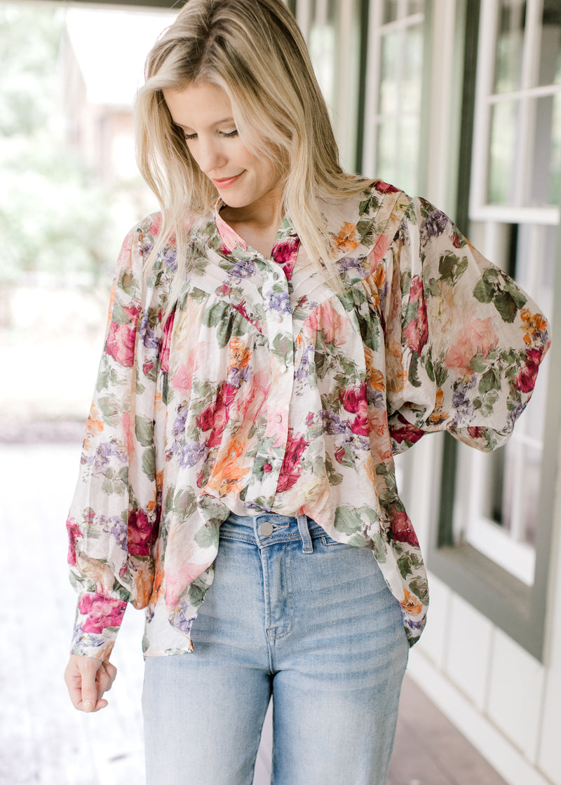 Model wearing jeans and a floral long sleeve top with a pleated bodice, and wide cuffs. 