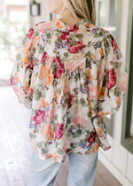 Back view of Model wearing a floral long sleeve top with covered buttons and wide cuffs. 