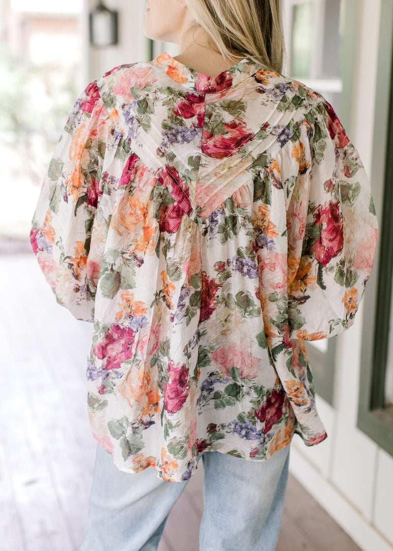 Back view of Model wearing a floral long sleeve top with covered buttons and wide cuffs. 