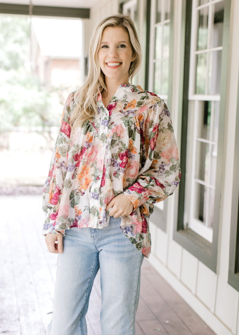 Model wearing a floral long sleeve top with a pleated bodice, covered buttons and a collar.