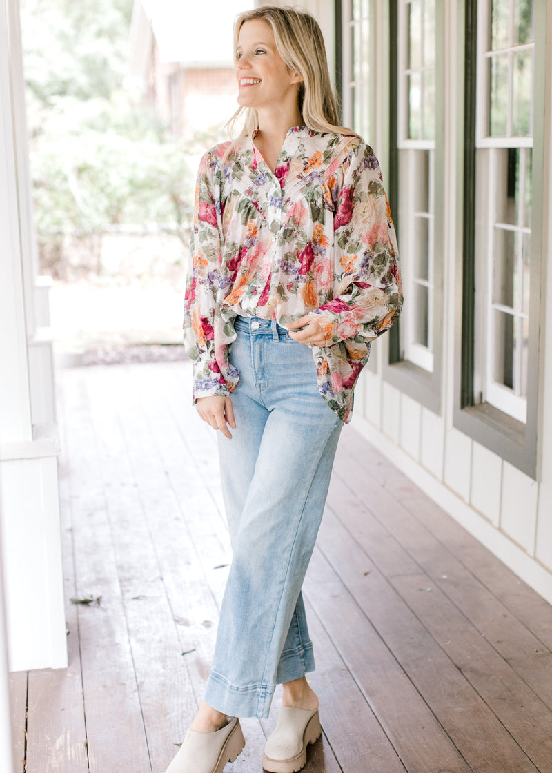 Model wearing jeans, mules and a floral long sleeve top with a pleated bodice and covered buttons. 