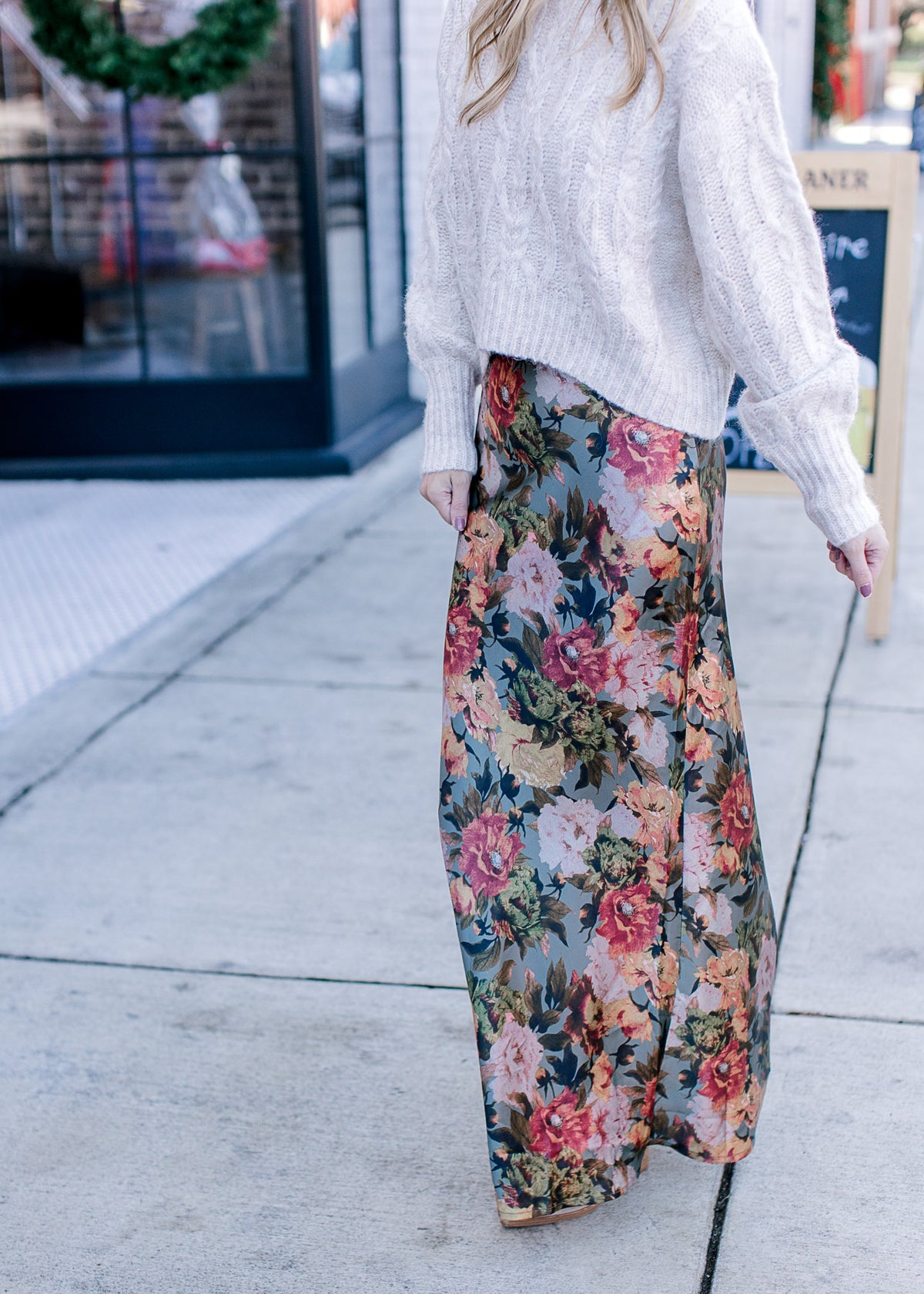 Model wearing a cream sweater and a deep sage silk fabric with warm floral and a hidden back zip.
