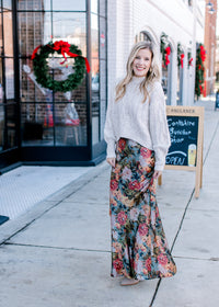 Model wearing a cream sweater, booties and  a silky sage maxi with warm floral.