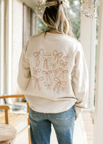 Back view of model wearing a cream sweatshirt with various bows and long sleeves.