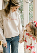 Model, with child, wearing a cream long sleeve sweatshirt with red “bind my wandering heart” script.