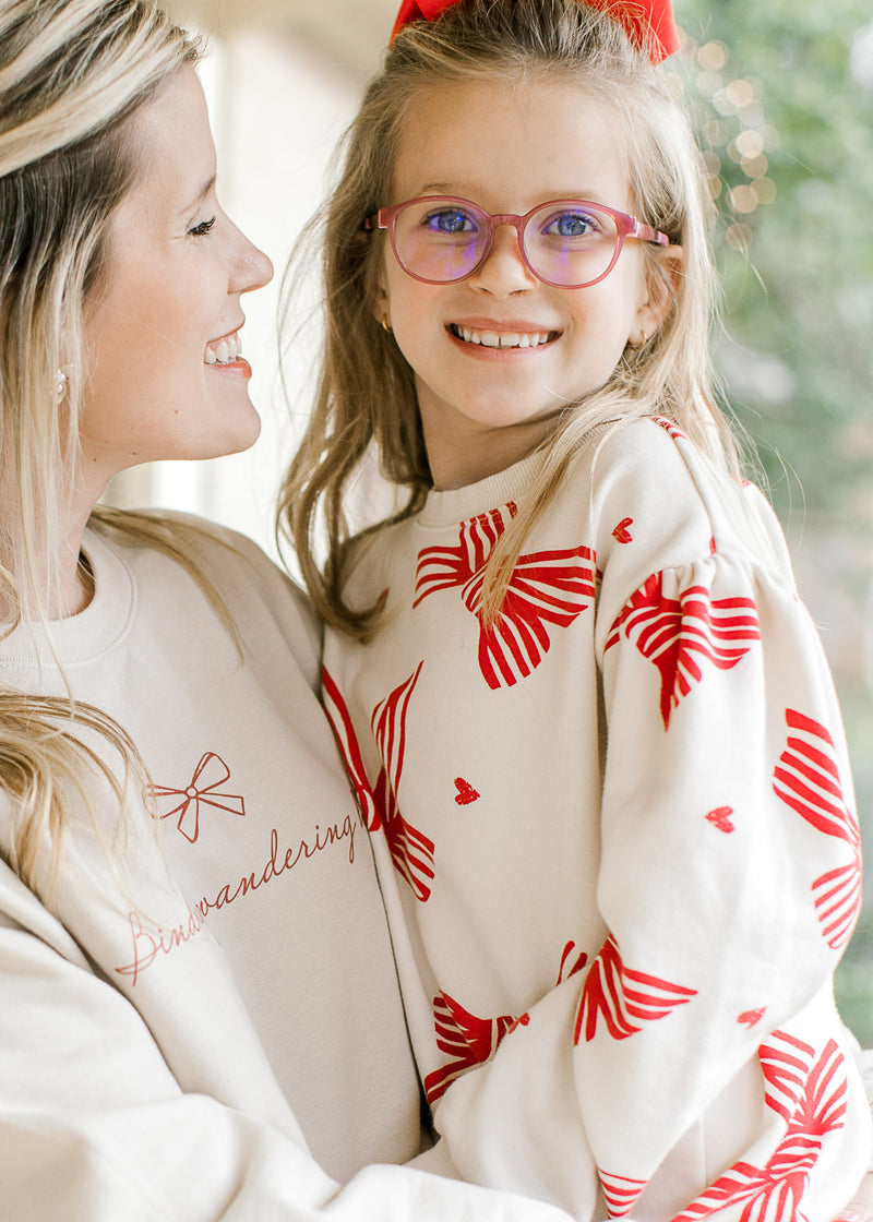 Model holding child while wearing a cream sweatshirt with red “bind my wandering heart” script. 