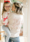 Back view of model holding child wearing a cream long sleeve sweatshirt with various bows.