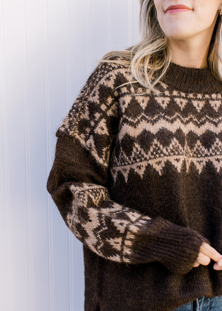 Model wearing a cozy brown sweater with tan geometric pattern, round neck and long sleeves. 