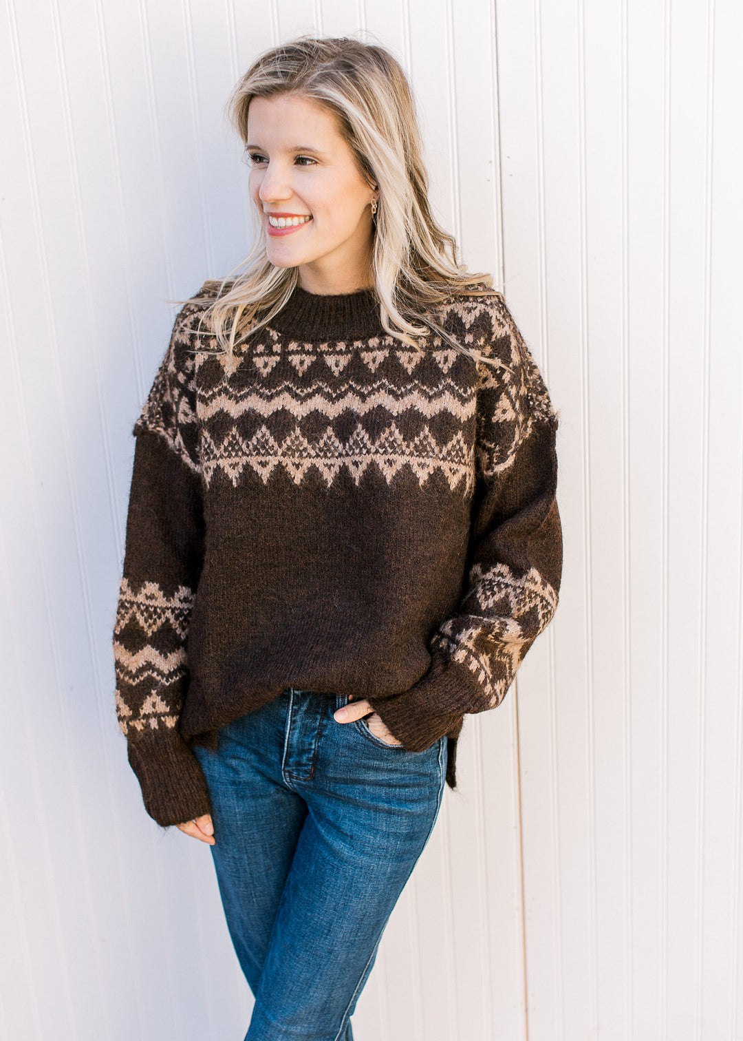 Model wearing jeans and a brown sweater with tan geometric pattern, round neck and long sleeves. 