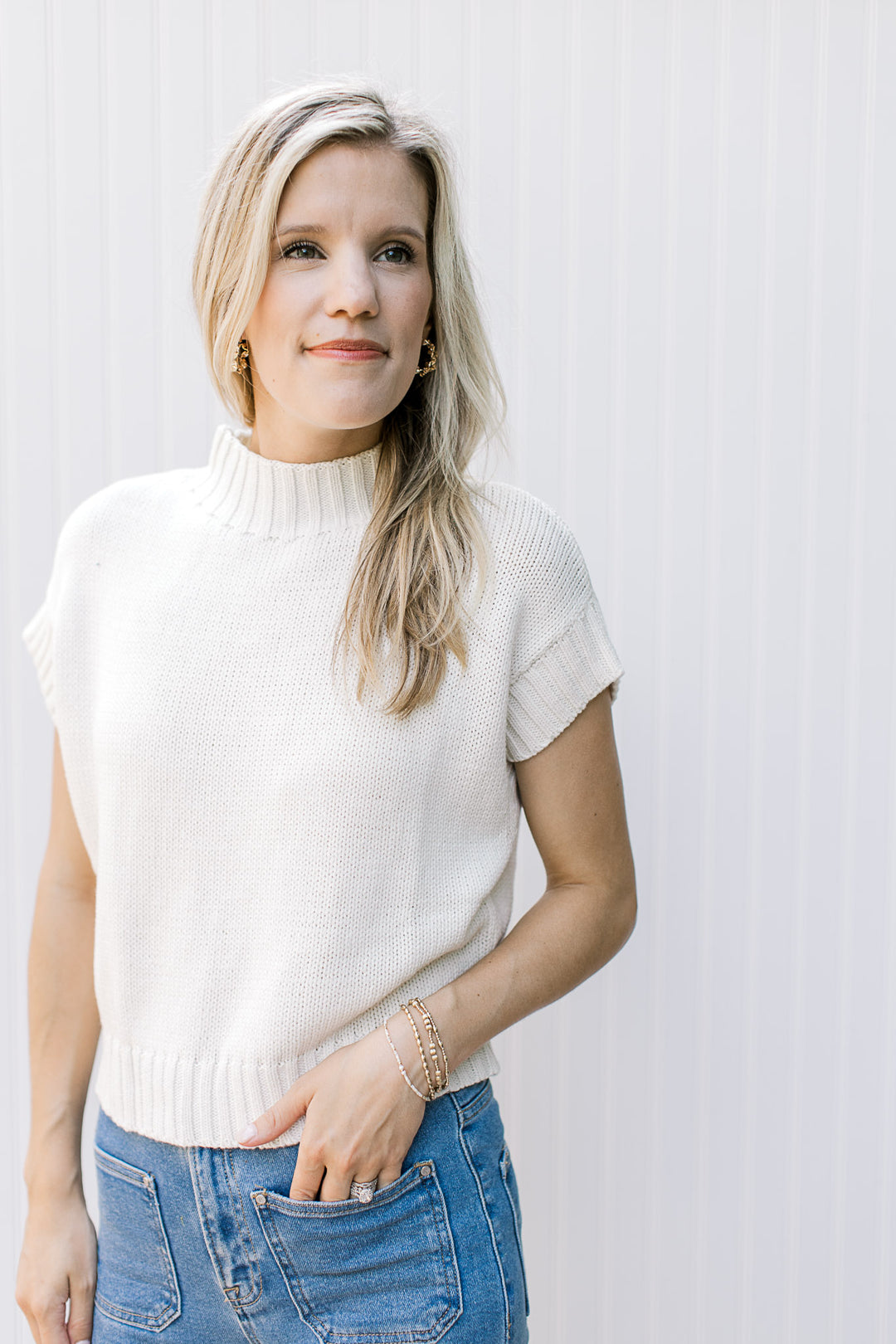 Model wearing a cream short sleeve sweater with a ribbed detail at neck, cuff and hem. 
