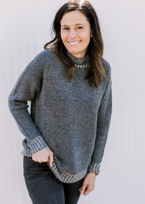 Model wearing a charcoal long sleeve sweater with light gray ribbing at neck, cuff and hem. 