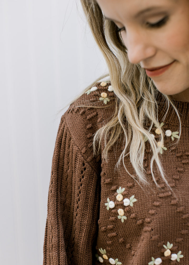 Close up of floral accents and diamond knit pattern on a mocha colored long sleeve sweater. 