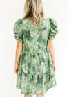 Back view of Model wearing a tiered dress with a green and cream pattern and layered short sleeve