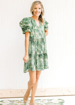 Model wearing flat mules with an above the knee, green and cream dress with layered short sleeves.