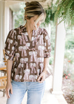 Model wearing a brown babydoll top with cream and mauve bows, v-neck and short sleeves.