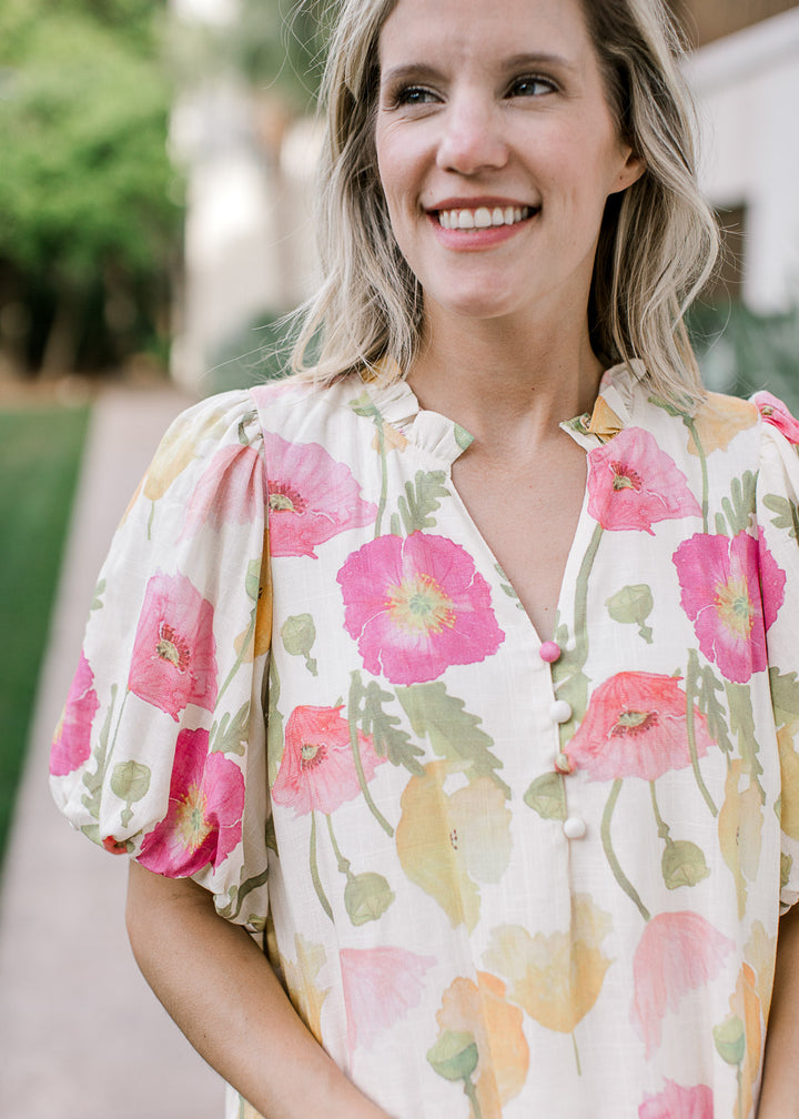Close p of v-neck with ruffle and bubble short sleeves on an above the knee cream dress with floral.