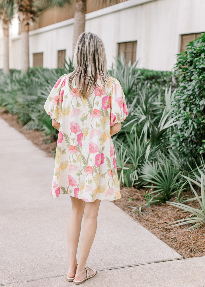 Back view of Model wearing a cream dress with pink and yellow floral, and bubble short sleeves.