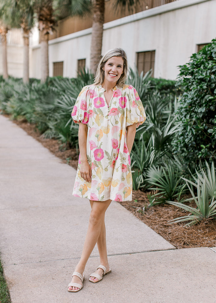 Model wearing sandals and a cream dress with floral, v-neck with buttons and bubble short sleeves.