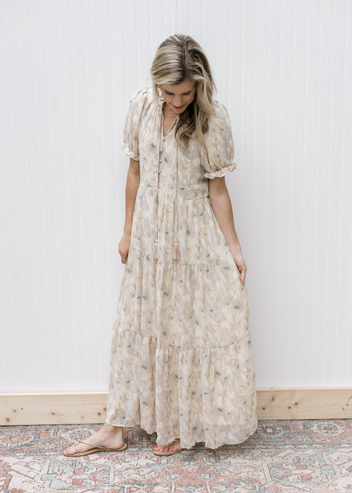 Model wearing a cream maxi with watercolor flowers, short sleeves with elastic and a tie v-neck.